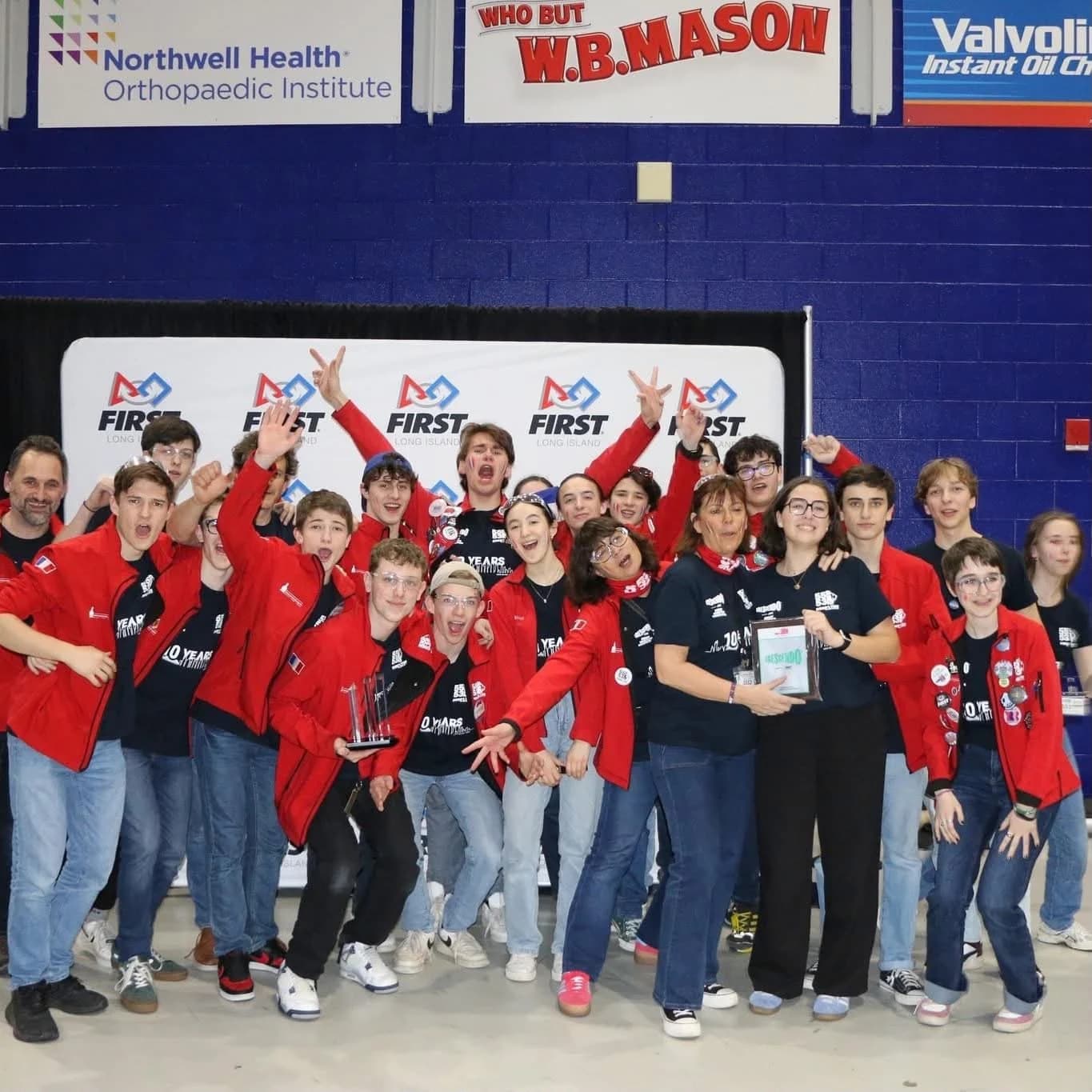 Équipe Robo’Lyon en veste rouge lors d’une compétition FIRST Robotics, rassemblée devant un panneau FIRST Long Island.